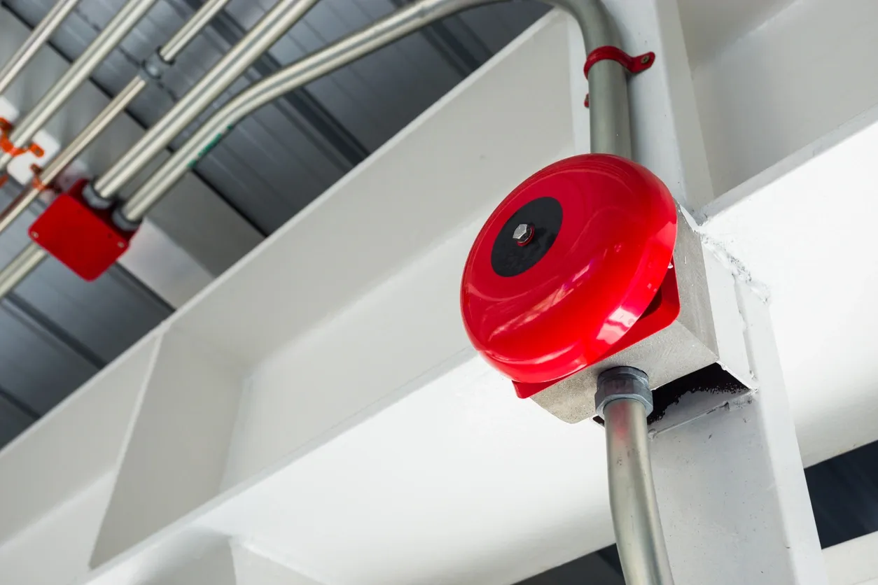 Red fire alarm bell on white beam